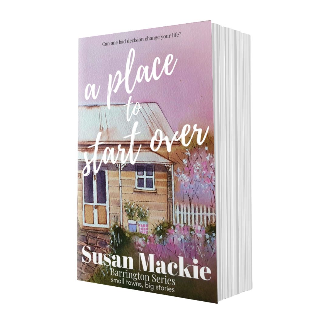 Book titled 'A Place to Start Over' by Susan Mackie with a watercolour painting of a cosy cottage.