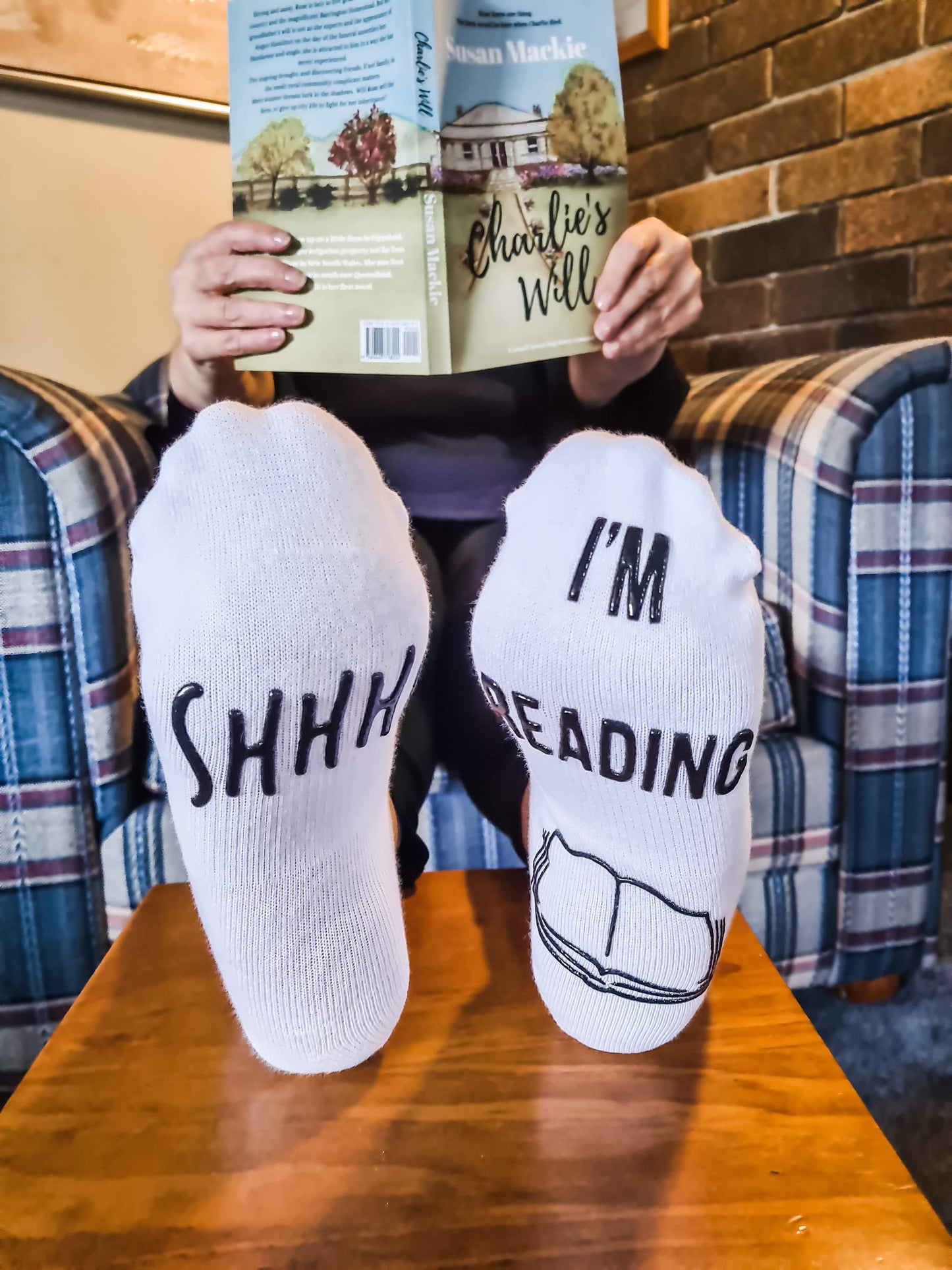 Person with reading socks holding a copy of Charlie's Will by Susan Mackie