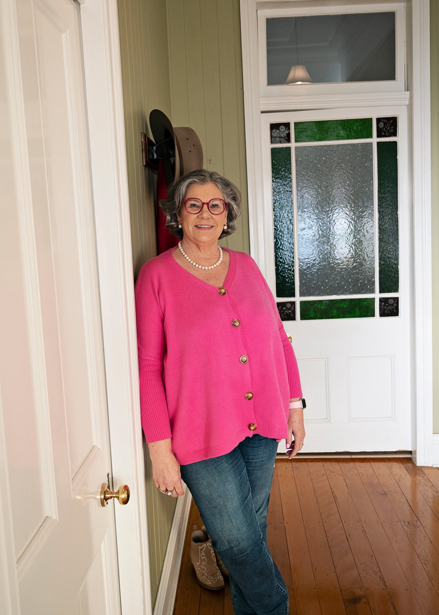 Author Susan Mackie in a pink sweater standing in a doorway with a white door with stained glass behind her.