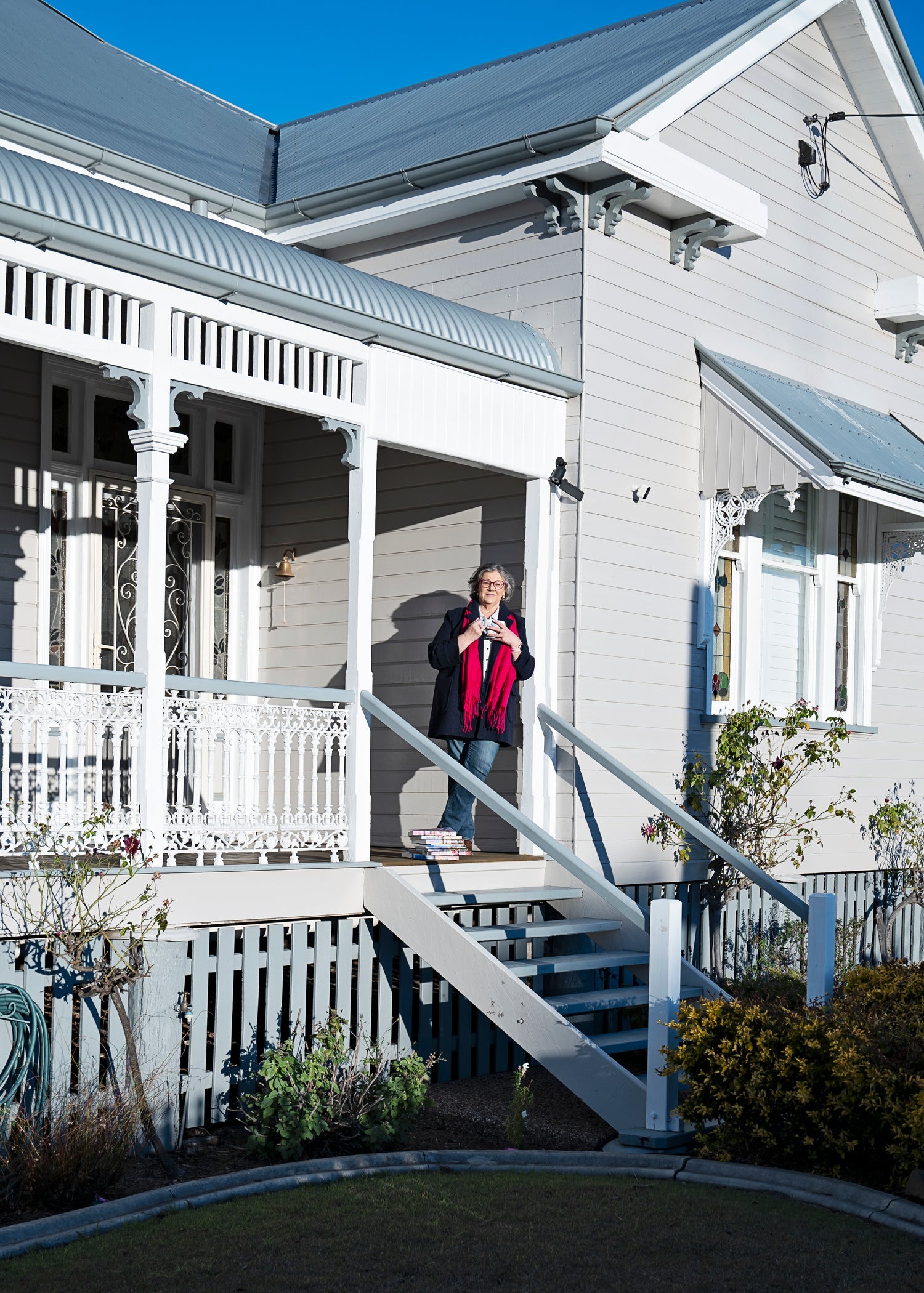 Author Susan Mackie standing on a porch of a white house with a blue sky.