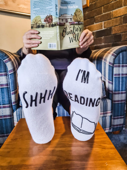 Person with reading socks holding a copy of Charlie's Will by Susan Mackie